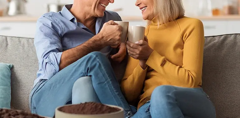 Couple in their 60s sharing steaming mugs on the couch